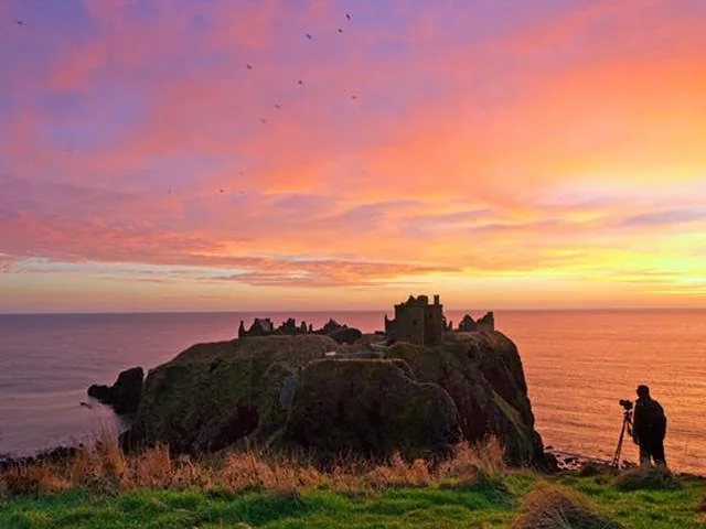 Fotograaf die een adembenemende zonsondergang vastlegt boven het silhouet van de ruïnes van Dunnottar Castle