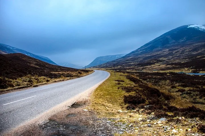 A winding road stretching through a vast, mountainous landscape under a cloudy sky