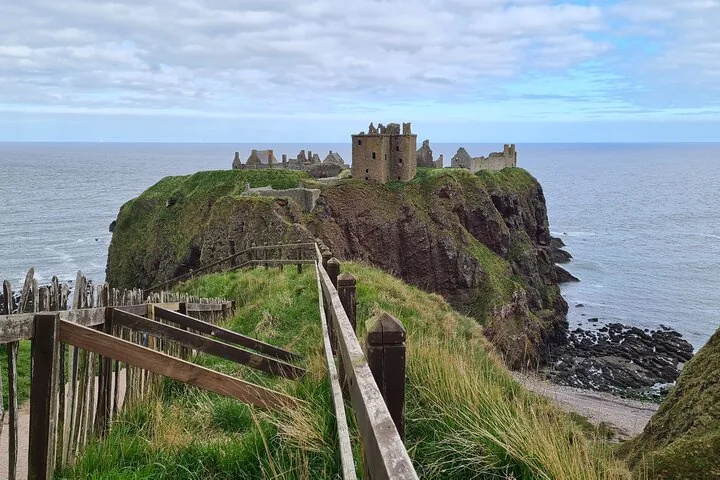 Houten hek langs een graspad dat naar Dunnottar Castle op de kliffen leidt