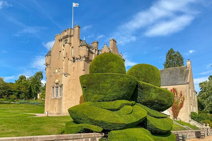 A historic castle with impressive sculpted topiary bushes in the foreground